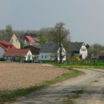 Der Kailaer Weg und der Ortseingang von Tausa. In der Mitte die beiden hellen Häuser, gehörten früher zum Schweinestall Tausa, der noch früher, also zu Zeiten des Gutes, die Schäferei war Der Kailaer Weg im Vordergrund und die ehemalige Schäferei bzw. der ehemalige Schweinestall im Hintergrund